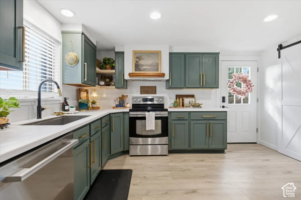 Kitchen featuring sage green cabinetry, brass hardware, wood-finish flooring, white countertops, and a sliding barn door