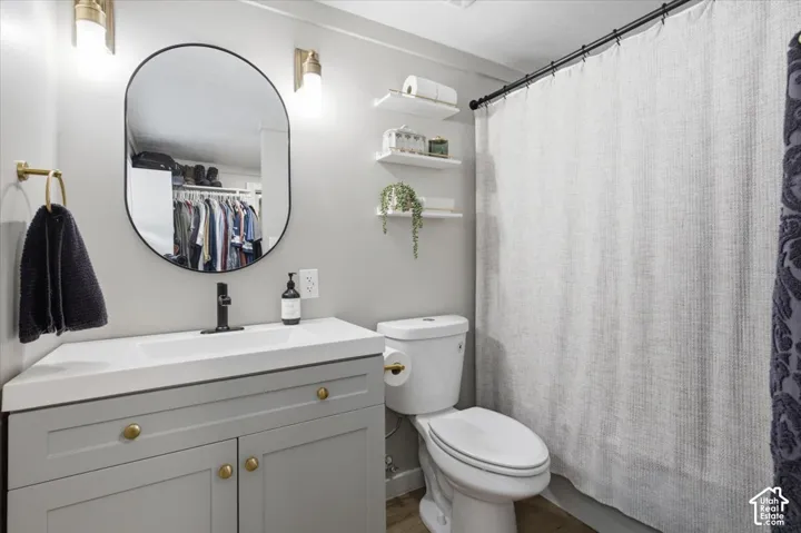 Grey shaker-style vanity with integrated rectangular sink and gold-tone hardware, paired with a matte black faucet, oval wall-mounted mirror, and wall-mounted light fixtures