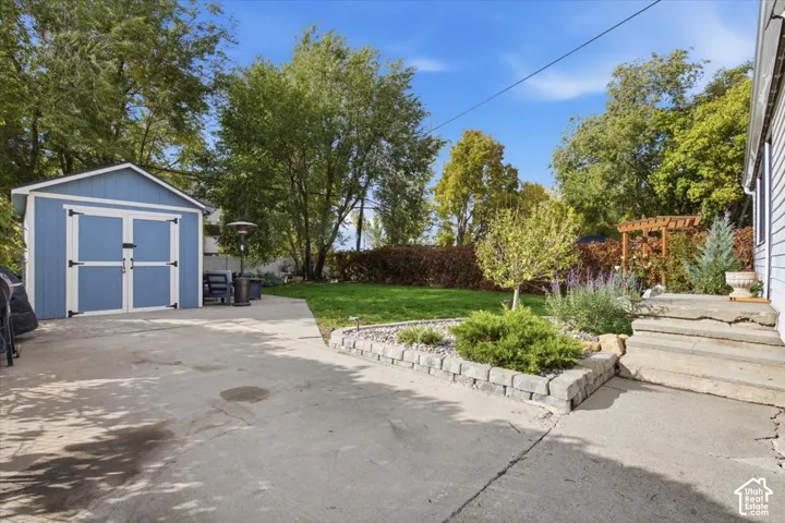 Backyard space featuring a concrete patio, detached storage shed, stone-bordered garden bed, lawn area, and wood-framed pergola