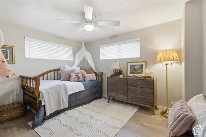 Neutral interior space featuring wood-finish flooring, two windows with horizontal blinds, and a white ceiling fan with integrated lighting