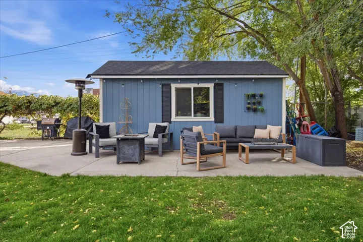 Detached structure with blue vertical siding, asphalt shingle roof, dark shutters, and a concrete patio