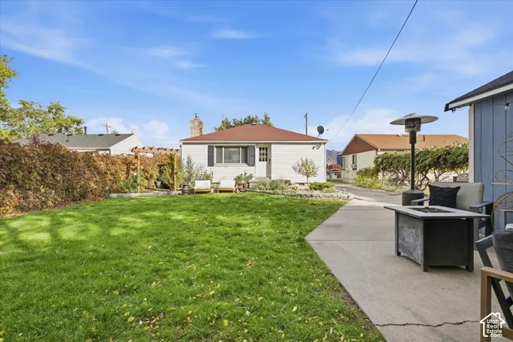 Backyard featuring a manicured lawn, concrete patio, stone garden border, and mature perimeter hedging