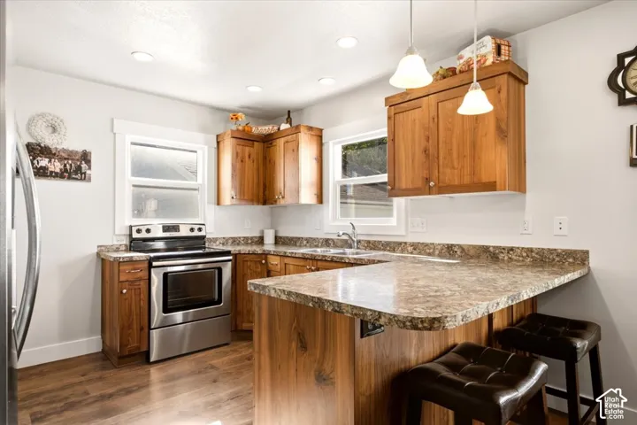 Kitchen featuring wood-finish cabinetry, stone-pattern laminate countertops, stainless steel range, wood-finish flooring, and pendant lighting