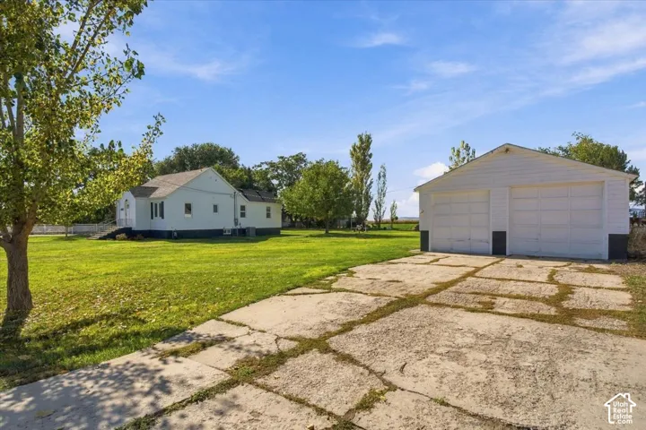 Expansive exterior grounds featuring a detached two-car garage, concrete driveway, and mature trees on a spacious parcel