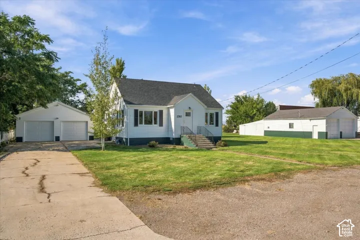 Single-story residence featuring a white exterior, dark shingle roof, two detached garages, and expansive lawn space