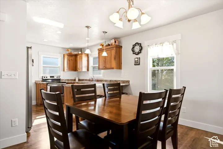 Kitchen featuring wood cabinetry, solid-surface countertops, wood-finish flooring, two hanging pendant lights, and a five-arm chandelier