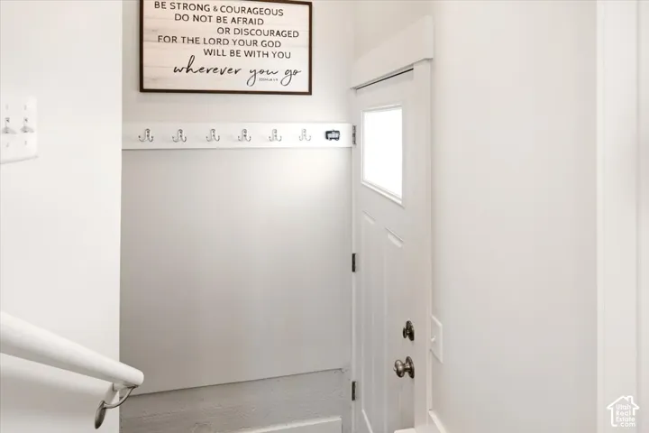 Entryway featuring a white paneled door with a rectangular glass insert, a wall-mounted hook rack, and a white handrail