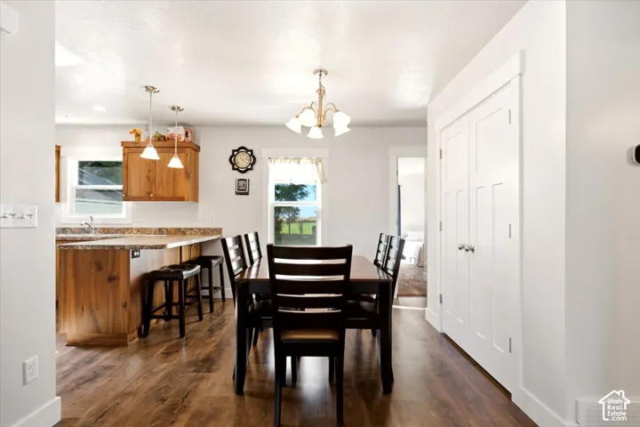 Kitchen featuring wood-finish cabinetry, stone-style countertops, wood-finish flooring, a multi-light chandelier, and a pair of white shaker-style doors