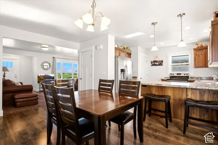 Kitchen featuring wood-finish cabinetry, stone-look countertops, stainless steel appliances, pendant lighting, and wood-finish flooring