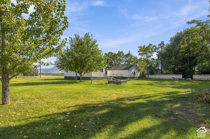 Expansive backyard featuring mature trees, a manicured lawn, white perimeter fencing, and a detached structure