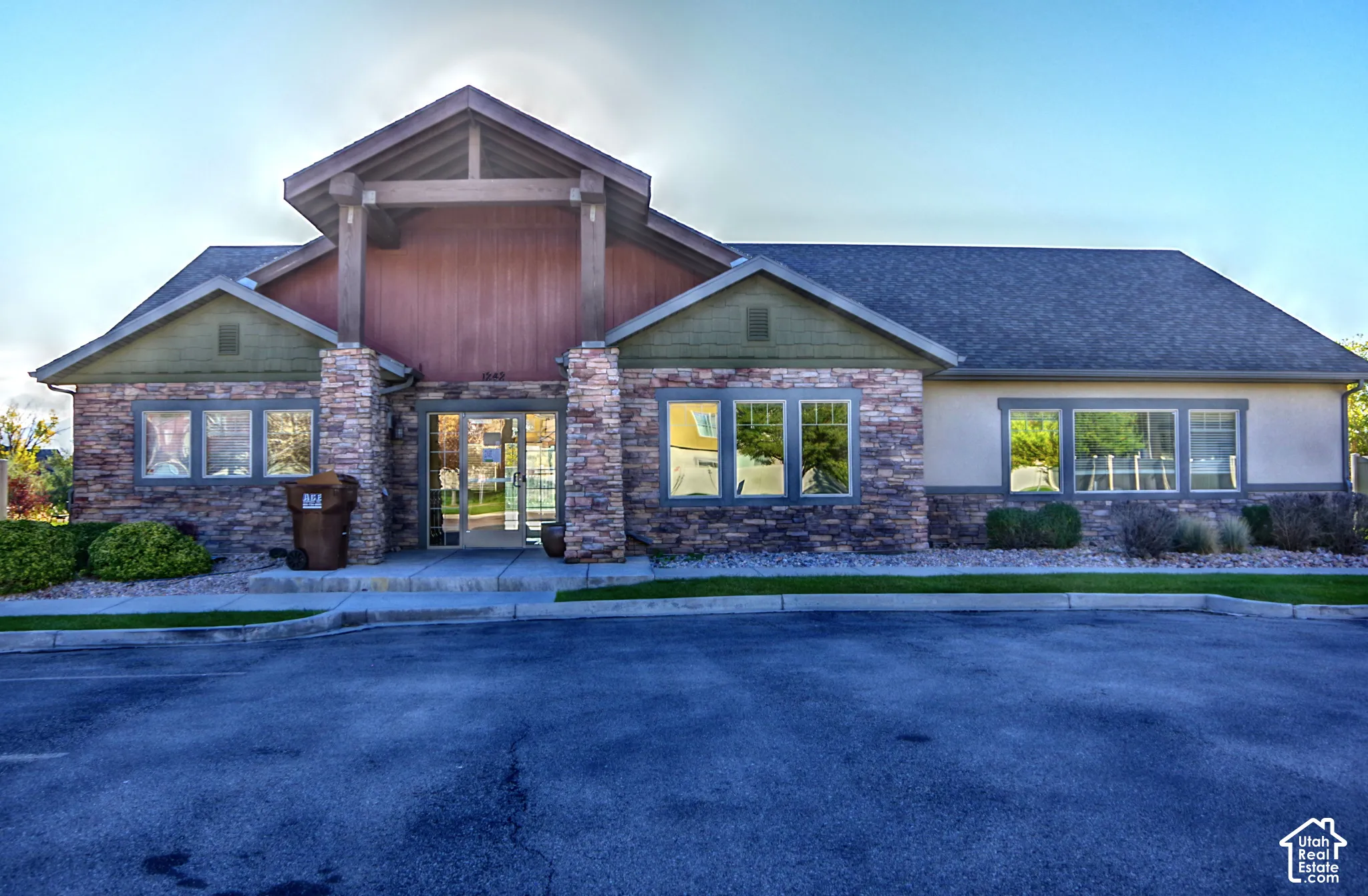 Exterior featuring stone veneer facade, wood-paneled gable detailing, shingle roof, and glass entry doors