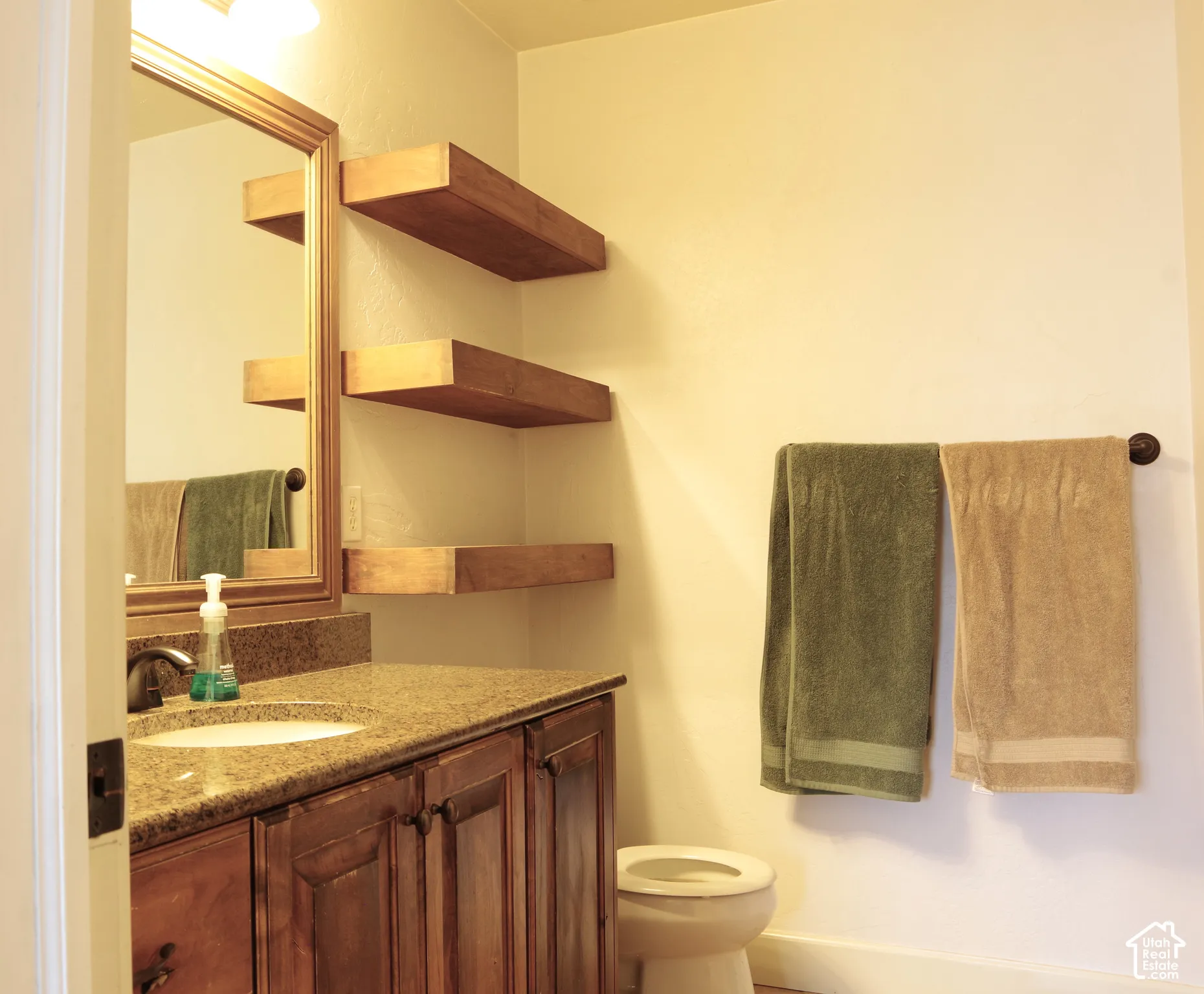 Bathroom vanity featuring wood cabinetry, stone-finish countertop, undermount sink, floating wood-finish shelving, and wall-mounted towel hardware