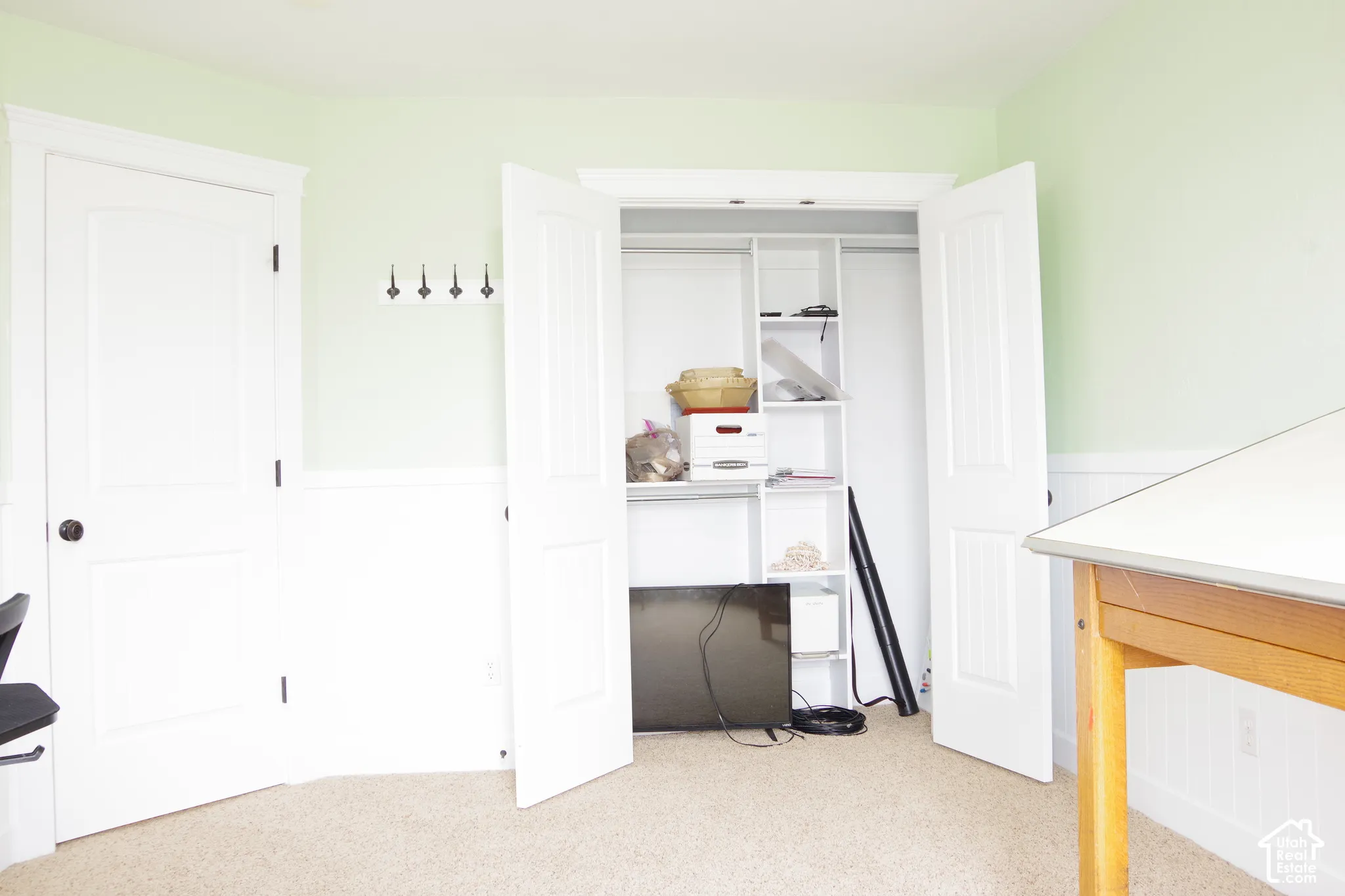 Room featuring wall-to-wall carpeting, beadboard wainscoting, a two-panel interior door, and a built-in closet with integrated shelving