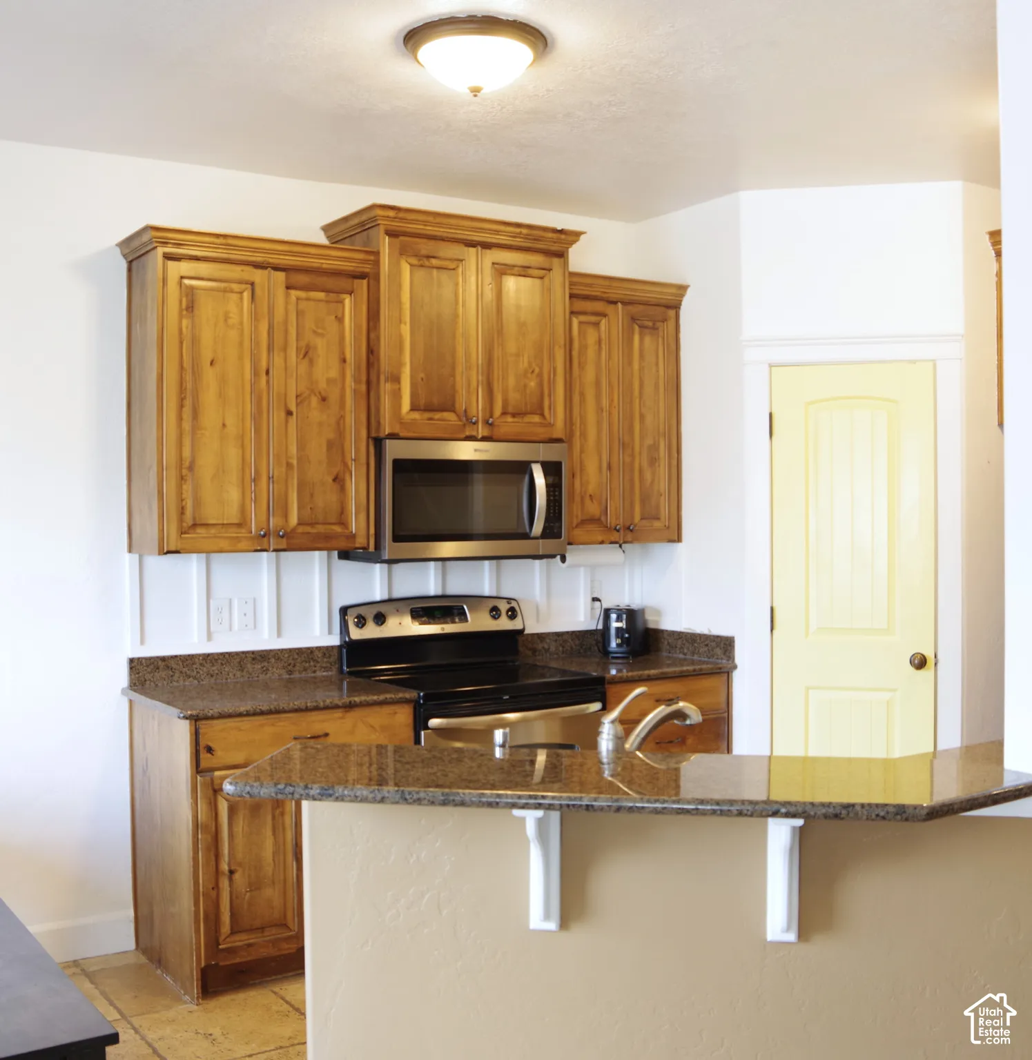 Kitchen featuring stained wood cabinetry, stone-finish countertops, stainless steel appliances, and a breakfast bar with decorative corbels
