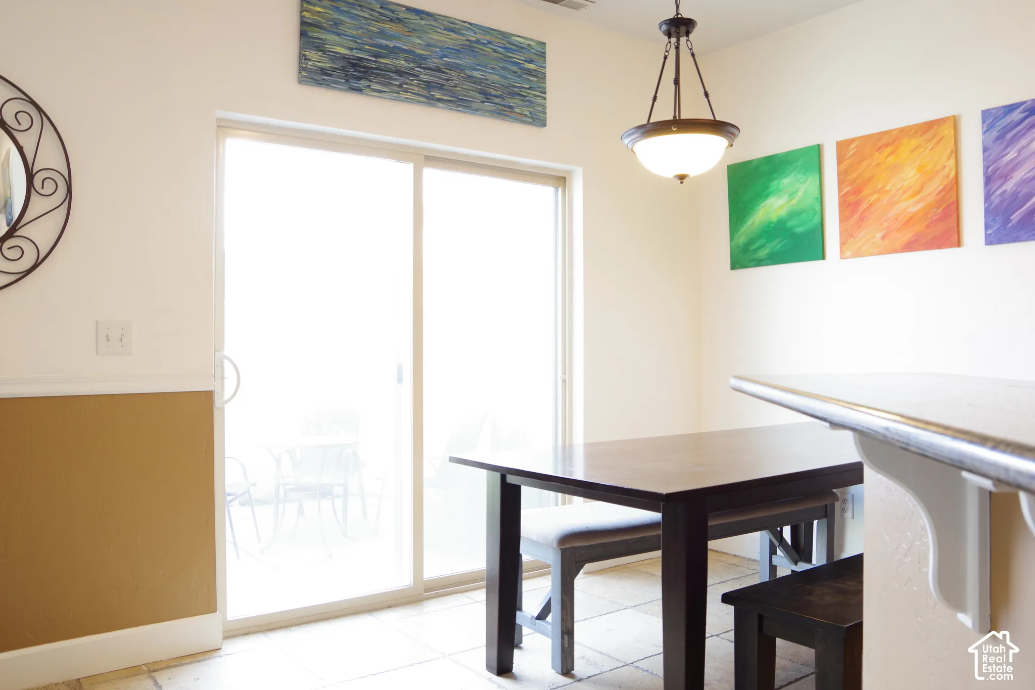 Sliding glass door, neutral-tone tile flooring, neutral wall paint with wainscoting, and a multi-light pendant fixture