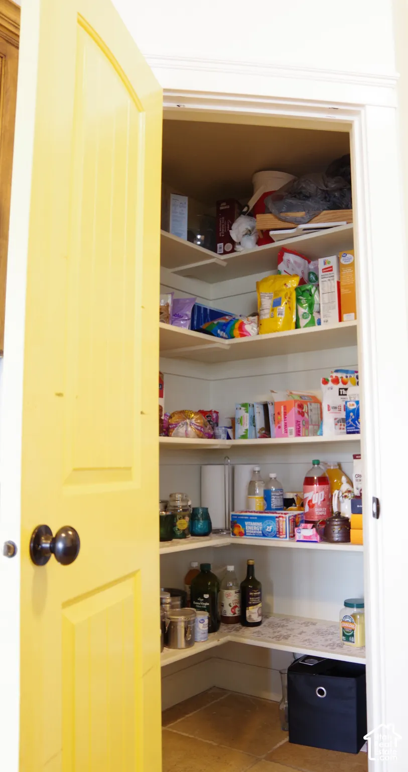 Pantry featuring five-tier corner shelving, shiplap-style wall paneling, tile flooring, and a solid-core panel door with a matte black round knob