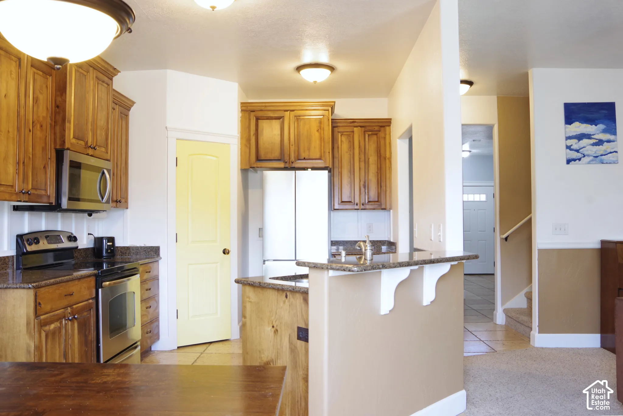 Kitchen featuring stained wood cabinetry, stone countertops, stainless steel appliances, and a breakfast bar with decorative corbel supports