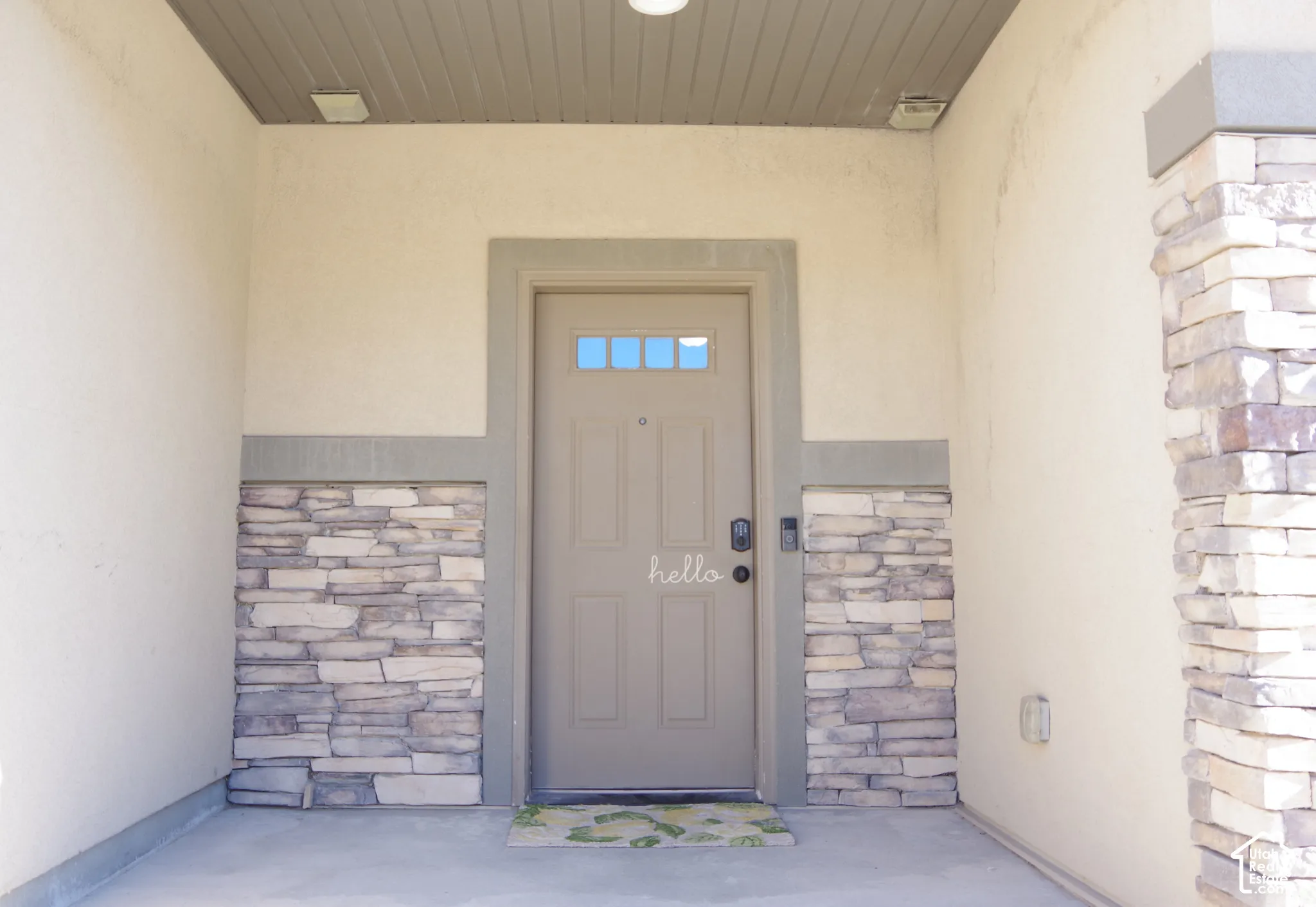 Covered entryway featuring smooth-finish stucco walls, stacked stone veneer accents, and a paneled entry door with a multi-pane glass inlay
