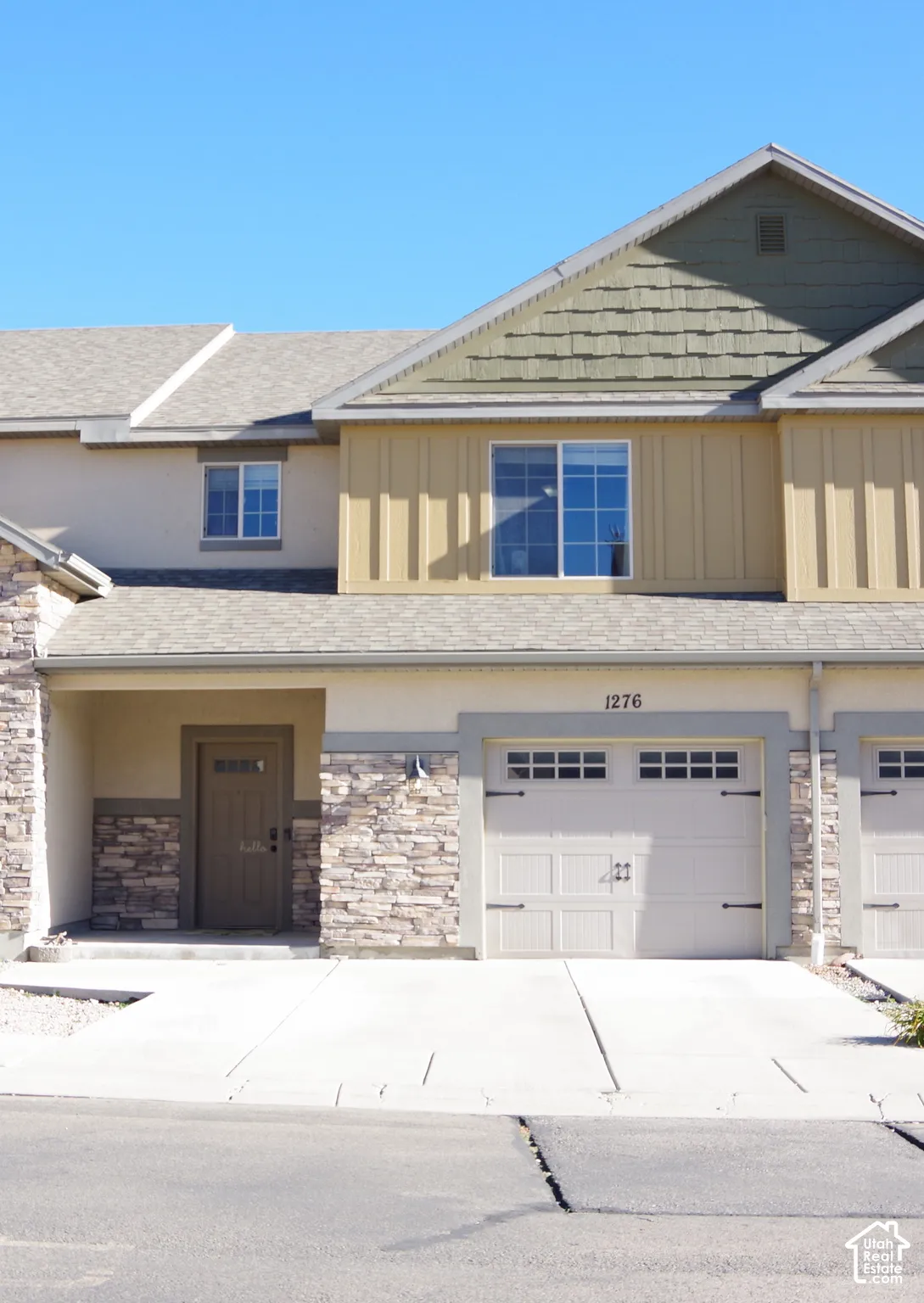 Exterior facade featuring stone veneer detailing, vertical siding, shingle-style roof accents, a covered entryway, and a multi-panel garage door