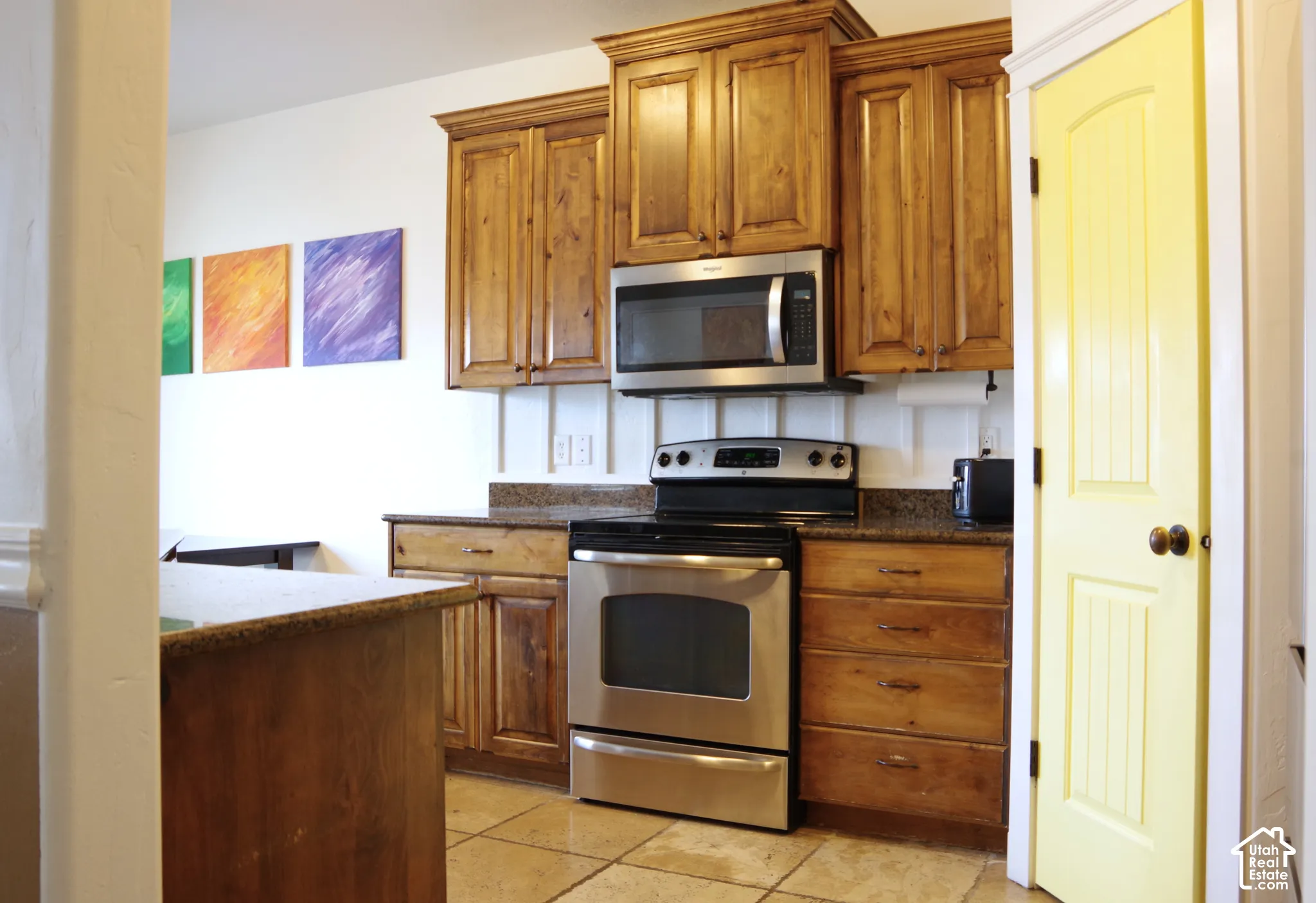 Kitchen featuring stained wood cabinetry, stone countertops, stainless steel appliances, a board and batten backsplash, and tile flooring