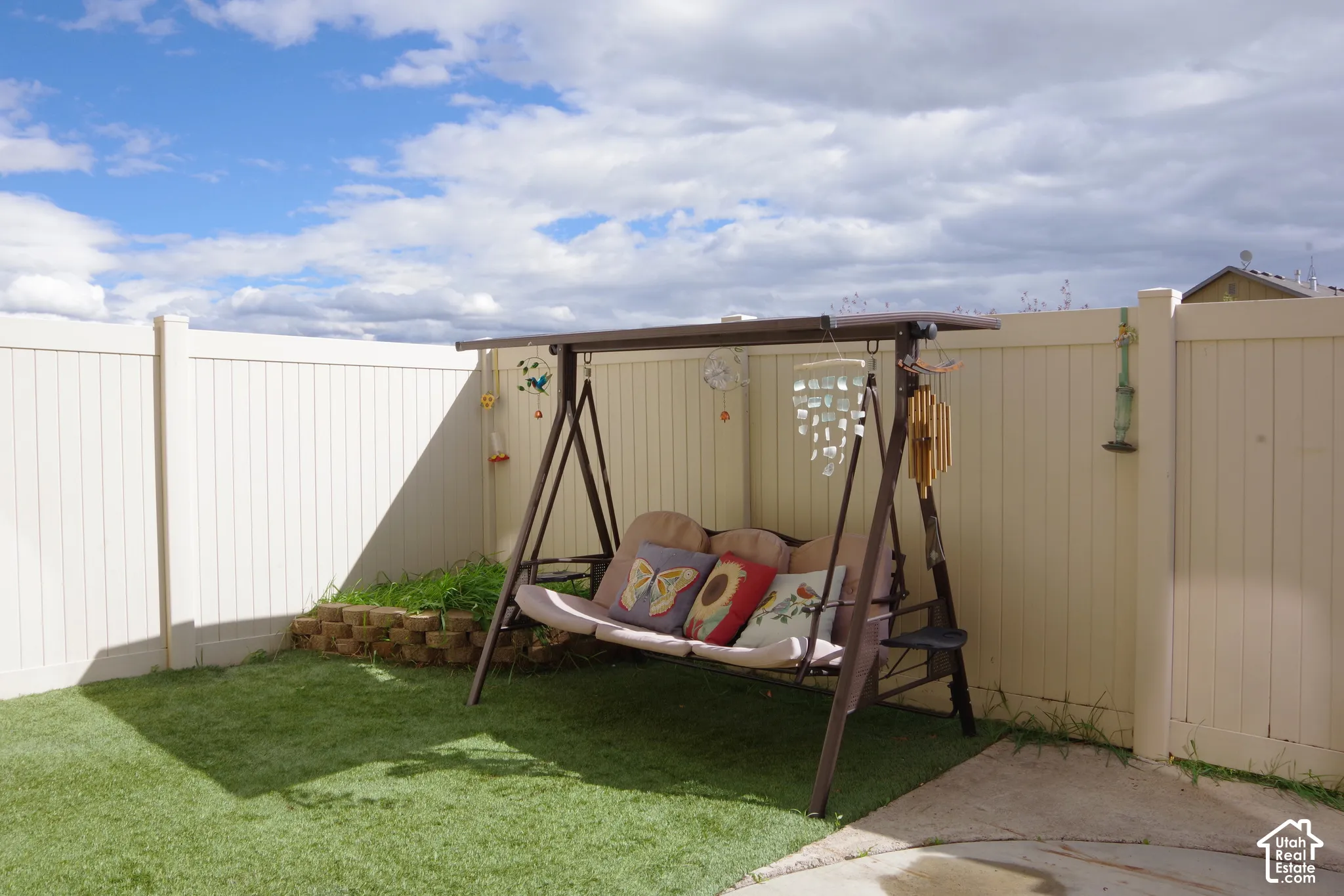 Backyard space featuring a solid-panel vinyl privacy fence, synthetic turf lawn, and a tiered stone retaining wall