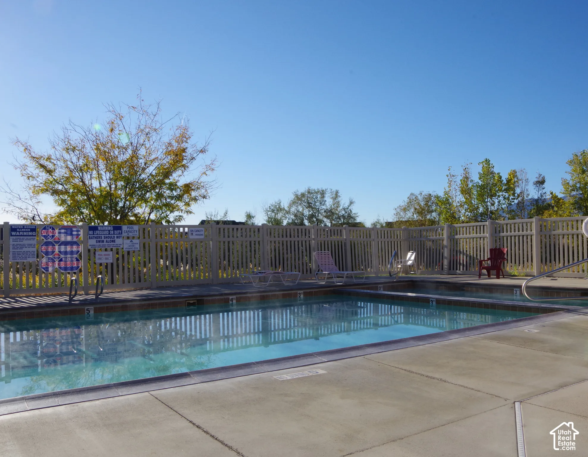 Swimming pool with a concrete deck, metal pool ladder, and vinyl privacy fencing