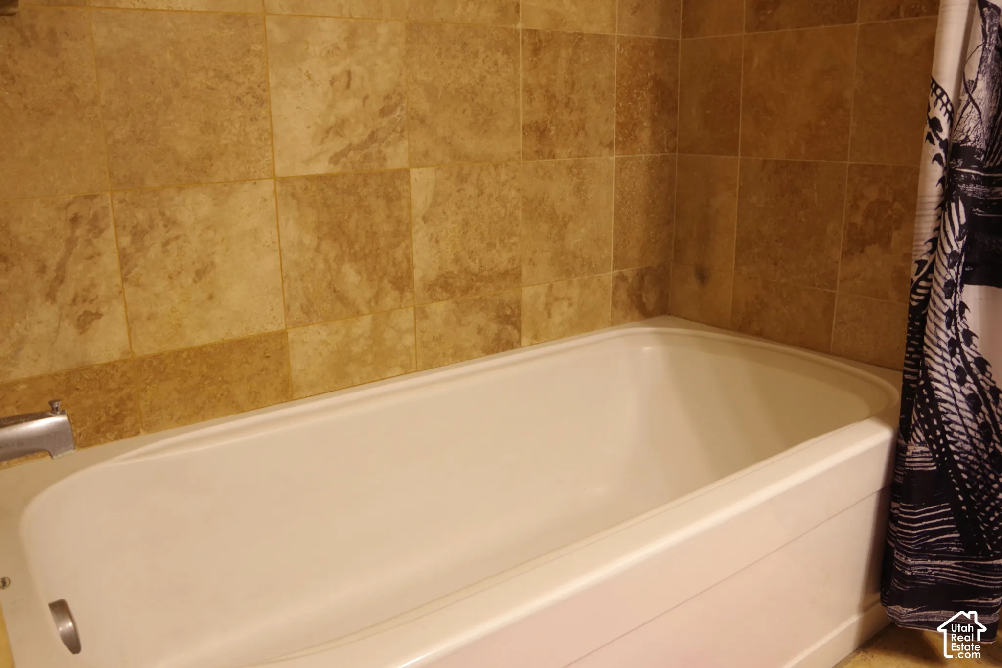 Bathtub featuring a white acrylic finish, chrome hardware, and full-height stone-finish wall tile