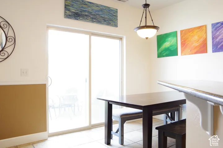 Sliding glass door, neutral-tone tile flooring, neutral wall paint with wainscoting, and a multi-light pendant fixture
