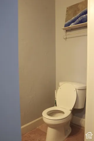 White vitreous china toilet with wall-mounted shelving unit and neutral stone-finish flooring