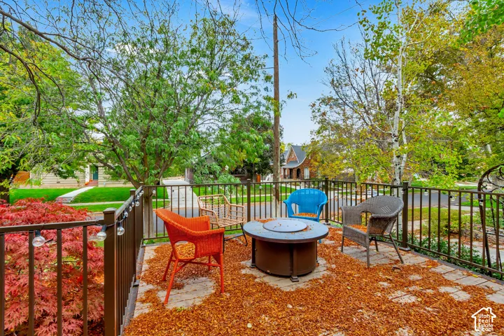 Elevated stone patio featuring metal railing, built-in fire pit, and mature landscape