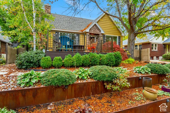 Yellow-sided exterior featuring an elevated deck with metal railing, stone-accented facade, and multi-tiered landscaping with steel retaining walls