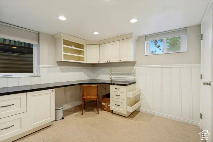 L-shaped built-in desk featuring dark stone countertops, custom white cabinetry, recessed lighting, and vertical wainscoting