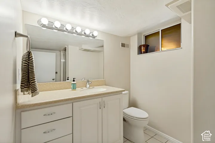 Bathroom featuring a white vanity with integrated basin, solid-surface countertop, multi-bulb vanity lighting, full-width wall mirror, and tile flooring
