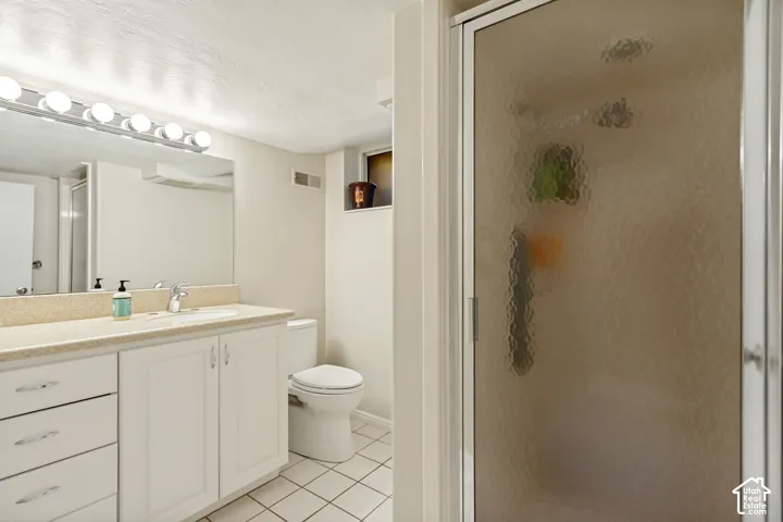 Bathroom featuring a white vanity with integrated countertop, large wall-mounted mirror, multi-bulb vanity lighting, and a shower with textured glass enclosure