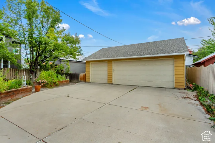 Detached three-car garage featuring horizontal siding, a composite shingle roof, and a paved concrete apron with raised garden beds