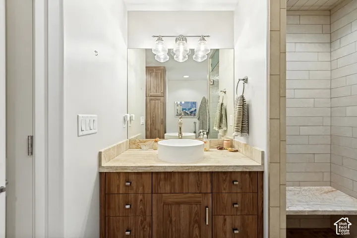 Custom wood-finish vanity with a stone countertop, circular vessel sink, three-light glass fixture, and walk-in shower with horizontal tile wall surrounds