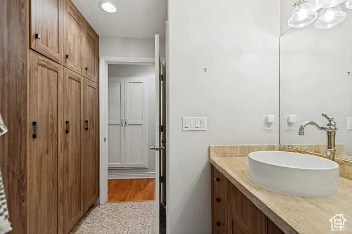 Full-height wood-finish cabinetry, stone countertop with a semi-recessed oval sink, polished metal faucet, and hexagonal patterned tile flooring