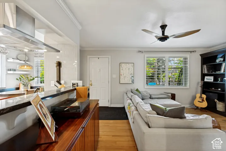 Kitchen featuring a breakfast bar with dark countertops, stainless steel vent hood, white subway tile backsplash, wood-finish flooring, and a modern ceiling fan