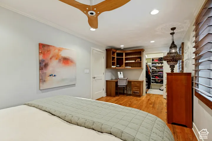 Wood-finish flooring, recessed lighting, three-blade ceiling fan, custom built-in wood desk with shelving, and walk-in closet with integrated storage