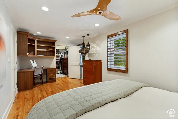 Wood-finish flooring, built-in wooden desk with integrated cabinetry, recessed lighting, wood-blade ceiling fan, and wooden window trim