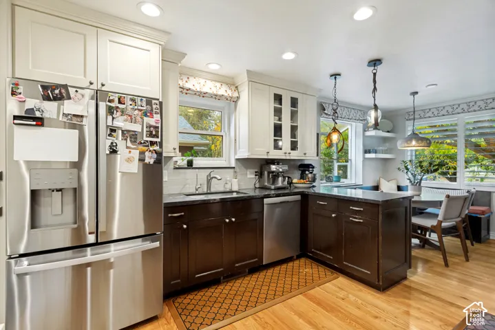 Kitchen featuring two-tone cabinetry, dark stone countertops, stainless steel appliances, wood-finish flooring, and multi-light pendant fixtures