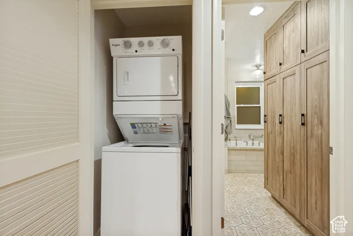 Laundry nook featuring a stacked washer and dryer, floor-to-ceiling cabinetry with wood-finish doors, and patterned tile flooring