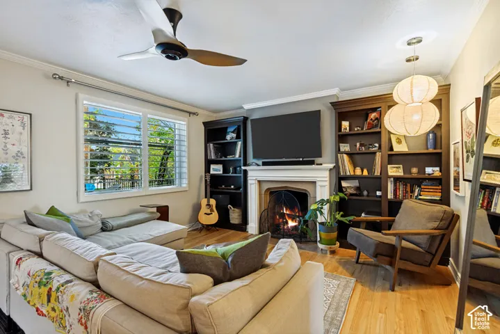 Living area featuring wood-finish flooring, a wood-burning fireplace with a traditional mantel, custom floor-to-ceiling built-in shelving, and a ceiling fan