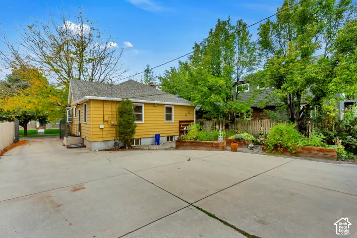 Exterior yellow siding with a concrete driveway and raised timber garden beds