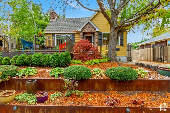 Exterior facade featuring horizontal lap siding, stone veneer entryway accents, a raised metal deck, tiered corten steel garden retaining walls, and mature landscaping