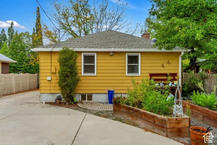 Yellow horizontal siding exterior with a hip roof, concrete driveway, and elevated wood-framed garden beds