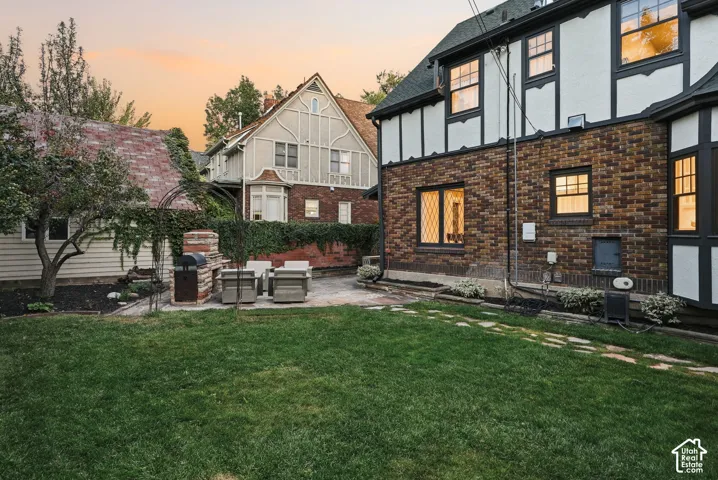 Tudor-style exterior featuring brick and half-timbered accents, stone-paved patio, masonry outdoor fireplace, and expansive lawn