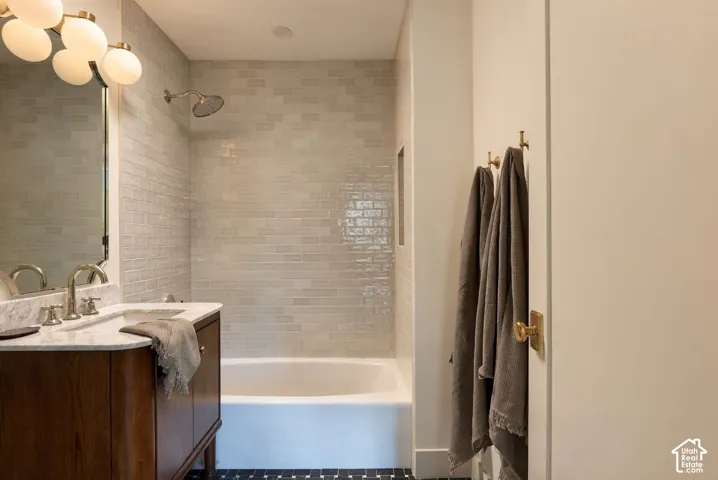 Bathroom featuring a dark wood-finish vanity with a stone countertop, an integrated sink with a metal faucet, polished metal wall-mounted light fixtures, a tub-shower combination with floor-to-ceiling subway tile surround, and a recessed wall niche