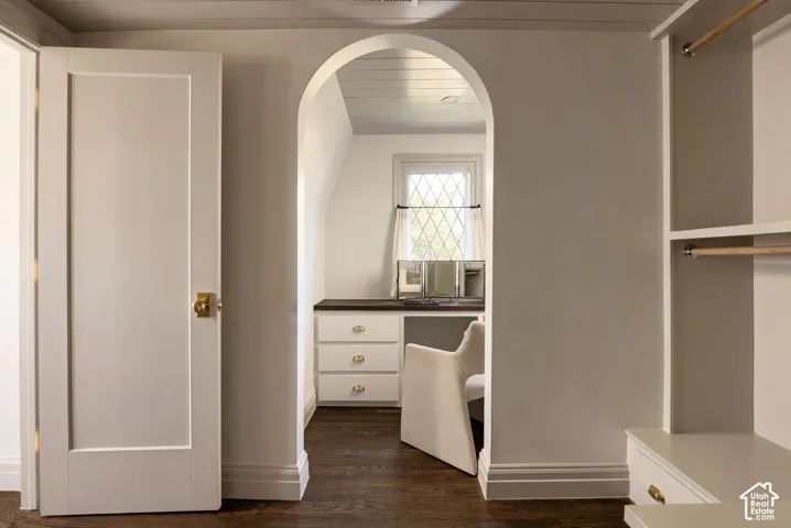 Arched doorway featuring wood-finish flooring, built-in cabinetry with metal hardware, recessed lighting, and a leaded glass window
