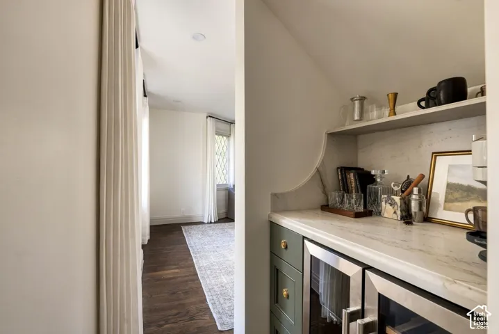 Built-in wet bar featuring custom olive-toned cabinetry, light-toned stone countertop with matching backsplash, brushed gold hardware, and recessed shelving